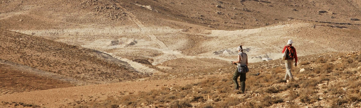 Panoramaaufnahme von zwei Forschenden in der Steppe, sie haben den Blick auf den Boden gerichtet und laufen von der Kamera weg