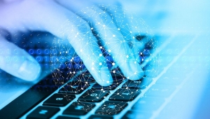 Hand bedient Computertastatur darüber schwebt eine transparente Darstellung einer Weltkugel, die voller Lichtpunkte ist, die mit Linien verbunden sind