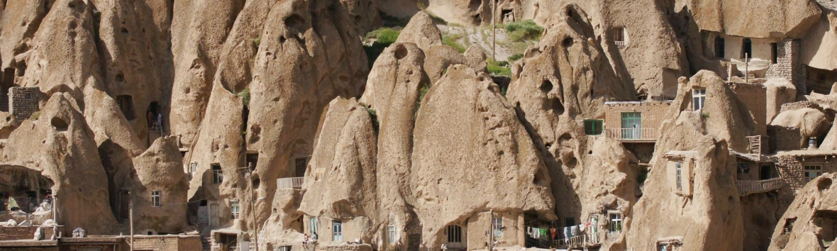 Foto von Felsenwohnungen. Die in den Fels eingearbeiteten Häuschen laufen kegelförmig zu, haben kleine Fensterlöcher und liegen eng beieinander.