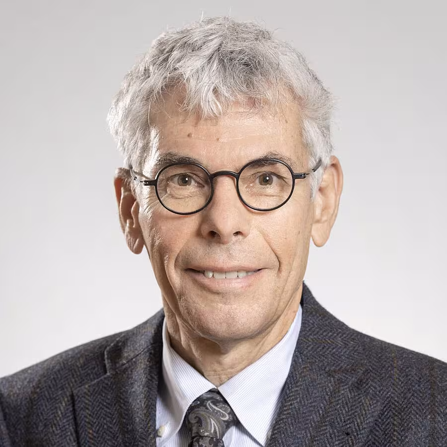 Brust-Porträt von Stefan Maul. Er trägt eine runde Brille hat kurze graue Haare und lächelt den Betrachter/die Betrachterin an. Er trägt ein Hemd, Krawatte und eine Anzugsjacke.