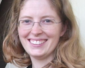 Porträt von Sara Landa in Nahaufnahme. Sie lächelt in die Kamera. Sara Landa trägt eine schwarze Bluse und eine Brille mit eckigen Gläsern. Die blonden Haare trägt sie offen.