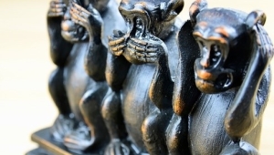 Drei aus Holz geschnitzte, schwarz bemalte Affenstatuen. Der linke Affe hält sich die Augen zu, der in der Mitte den Mund und der rechts die Ohren.