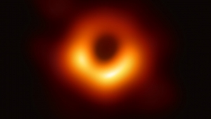 Bild eines schwarzen Lochs. Vor schwarzem Hintergrund ist ein roter, feuerartiger Ring zu sehen. In der Mitte des Rings befindet sich ein schwarzer Kreis.