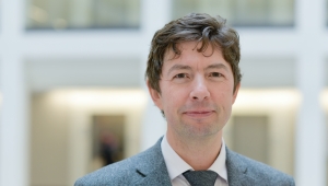Frontalansicht bis zur Brust von Christian Drosten, der den Betrachter freundlich anblickt. Er trägt einen Anzug mit Krawatte und hat kurze dunkelbraune Haare. 