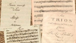 Zwei Notenblätter und zwei Titelblätter der Musikstücke liegen auf einem hellbraunen Untergrund.