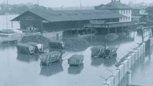 Schwarz-weiß Foto des Elbehochwassers im Januar 1932: Die Elbe tritt in der Nähe von Dresden über ihre Ufer (Bundesarchiv, Bild 102-12896, anonymes undatiertes Foto); zu sehen sind ein längliches Gebäude und einige Kutschwagen, deren Räder im Wasser stehen.