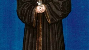 Bildnis von Melanchthon. Er ist vor einem dunkelblauen Hintergrund abgebildet und steht auf hellem Grund. Melanchthon blickt nach links an den Betrachtenden vorbei. Er trägt einen knöchellangen, schweren Mantel mit braunem Pelzbesatz in der Mitte. Dazu trägt er schwarze Schuhe. In der Hand hält er eine Papierrolle. Auf dem Kopf trägt er ein Barett.