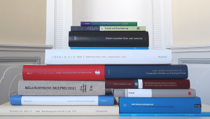 Bücherstapel, der die Buchrücken der Bücher zeigt und nach oben hin spitz zuläuft. Die Bücher sind unterschiedlich groß, dick und haben verschiedene Farben. Es sind Ausgaben aus den Publikationsreihen der Akademieprojekte.