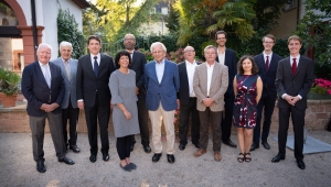 Gruppenbild im Garten der HAdW, im Hintergrund sind grüne Pflanzen zu sehen, davor stehen 12 Personen in zwei Reihen zusammen, sie tragen feierliche Kleidung und lächeln in die Kamera, die 10 Männer tragen dunkle Anzüge, eine Frau in der ersten Reihe links ein graues Kleid, eine Frau in der Resten Reihe rechts ein blaues Kleid mit rotem Blumenmuster
