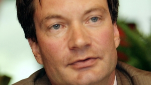 Portrait von Volker Wulfmeyer in Nahaufnahme. Er schaut leicht am Betrachter vorbei und hat den Mund leicht geöffnet. Er trägt ein braunes Jackett, darunter ein weißes Hemd und eine gestreifte Krawatte.