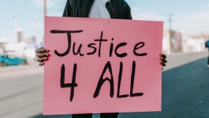 Pinkes Plakat gehalten von einer schwarzen Person mit der Aufschrift "Justice 4 ALL"