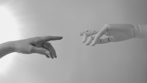 Auf dem Bild sind eine menschliche Hand und eine Roboterhand zu sehen, die sich zueinander hinstrecken. Die Fingerspitzen berühren sich fast. Das Bild ist angelehnt an Michelangelos Die Erschaffung Adams, wo Gott und Adam ihre Hände in gleicher Weise zueinander hinstrecken.