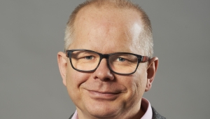 Frontalansicht bis zur Brust von Jörg Schmalian, der mit einer Brille den Betrachter anlächelt. Er trägt ein Hemd  mit Weste und darüber eine Anzugsjacke. 