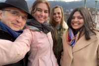 vier Personen in Winterkleidung auf einem Selfie. Links ein Mann mit schwarzem Mantel und Hut, daneben eine Frau in hellrosa Jacke, die den rechten Arm zum fotografieren nach vorne ausgesteckt hat. Rechts davon eine weitere Frau im dunklen Parka. Ganz rechts eine dritte Frau in beigem Mantel und mit buntem Schal. Alle vier lächeln in die Kamera.