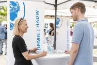 Zwei Personen im Gespräch. Im Hintergrund ist das Logo der Akademie zu sehen. 